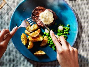 beef filet with blue cheese butter on top and potato wedges and peas on blue plate