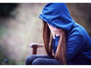 Teenage girl in hooded top with head in hands in despair