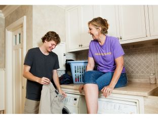 teen boy doing laundry while mother watches