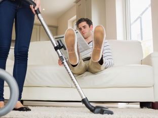 Man raising his feet while woman cleaning in living room
