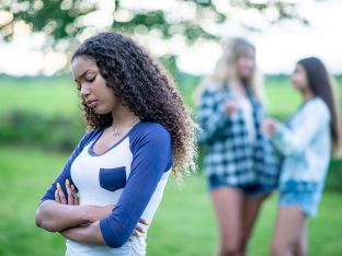 Two teen girls in the background making fun of or bullying a third girl