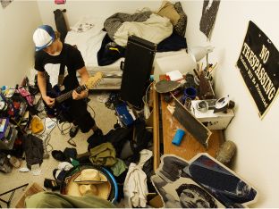 teen playing guitar in extremely messy bedroom