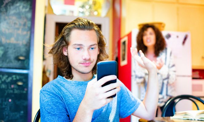 Male teenager ignoring scolding mom with mobile phone