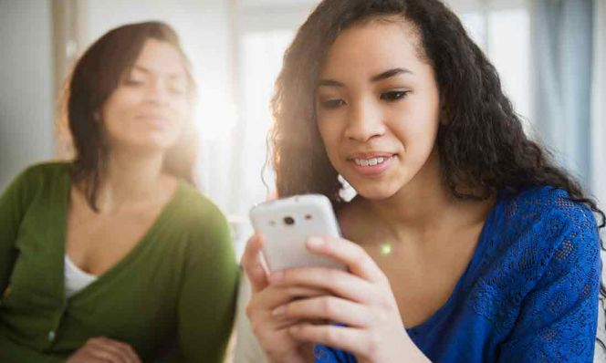 Mother watching daughter use cell phone
