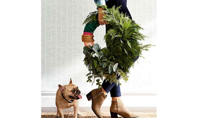 woman carrying a holiday wreath with dog watching