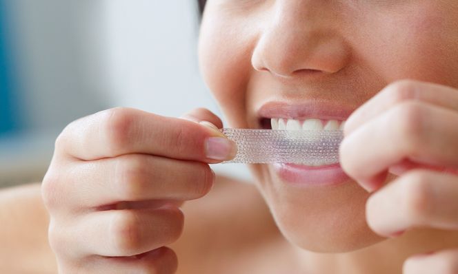 woman applying white strips to teeth